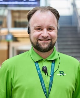 Employé portant un polo vert avec logo “R”, un casque et un lanyard.