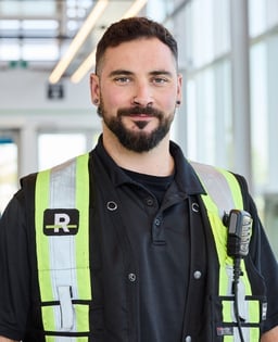Personne en gilet de sécurité avec radio, dans un environnement intérieur vitré.