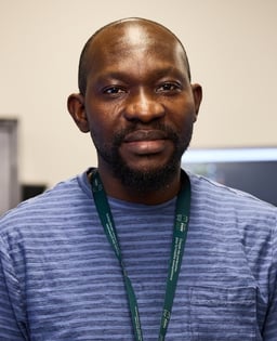 Personne portant une chemise rayée bleue et un lanyard vert.