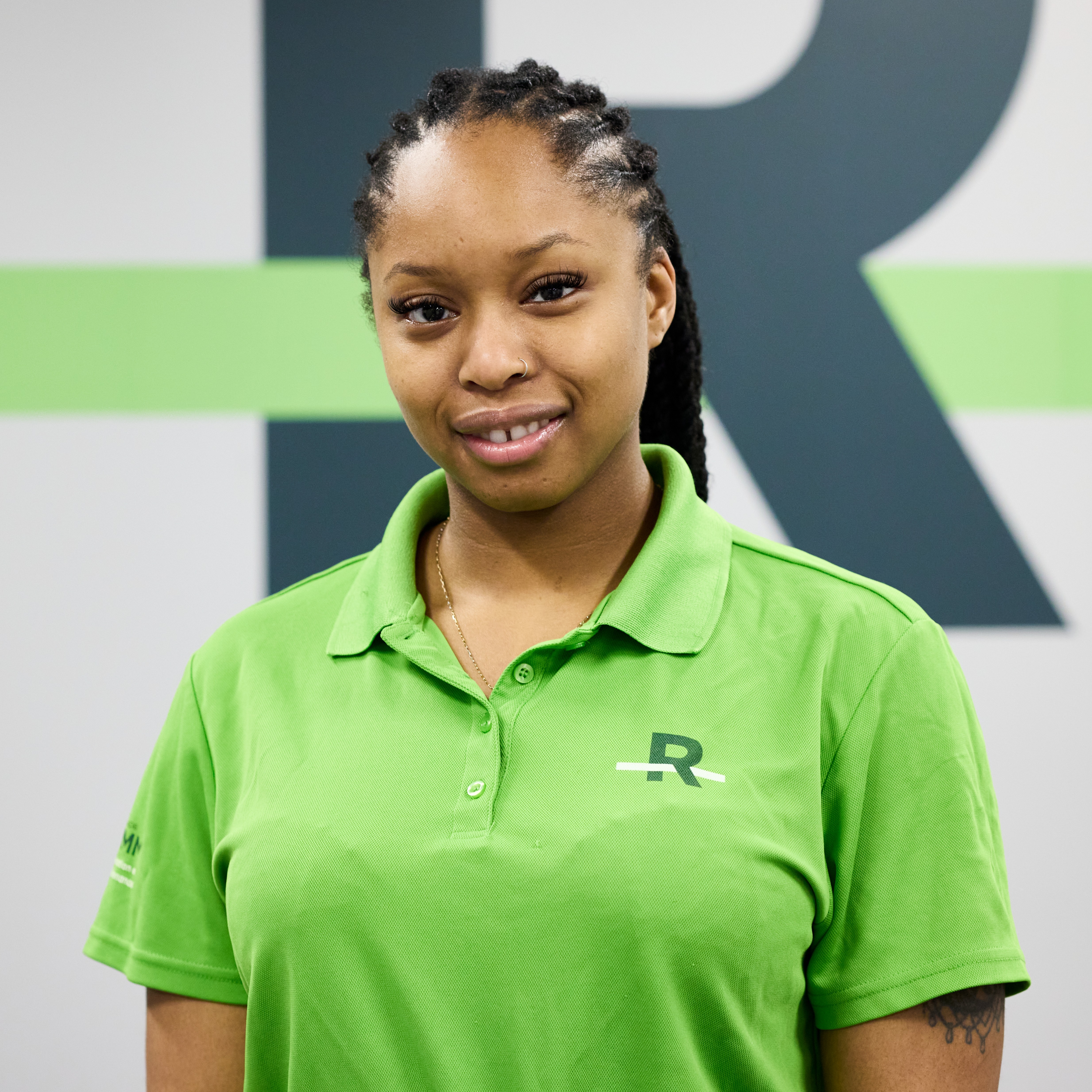 Personne en polo vert avec logo « R », devant un mur assorti.