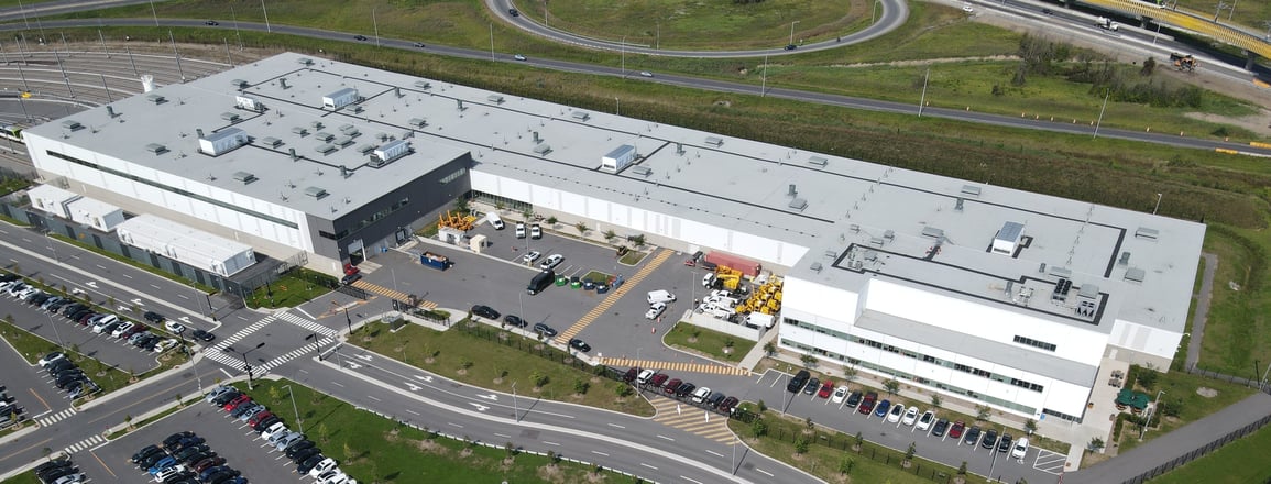 Vue aérienne d’un grand bâtiment commercial avec stationnement, routes et voie ferrée.