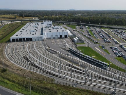 Vue aérienne d’un dépôt ferroviaire avec trains, stationnement et bâtiments.