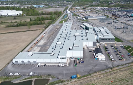 Vue aérienne d’un site industriel avec bâtiments, stationnements et lignes électriques.